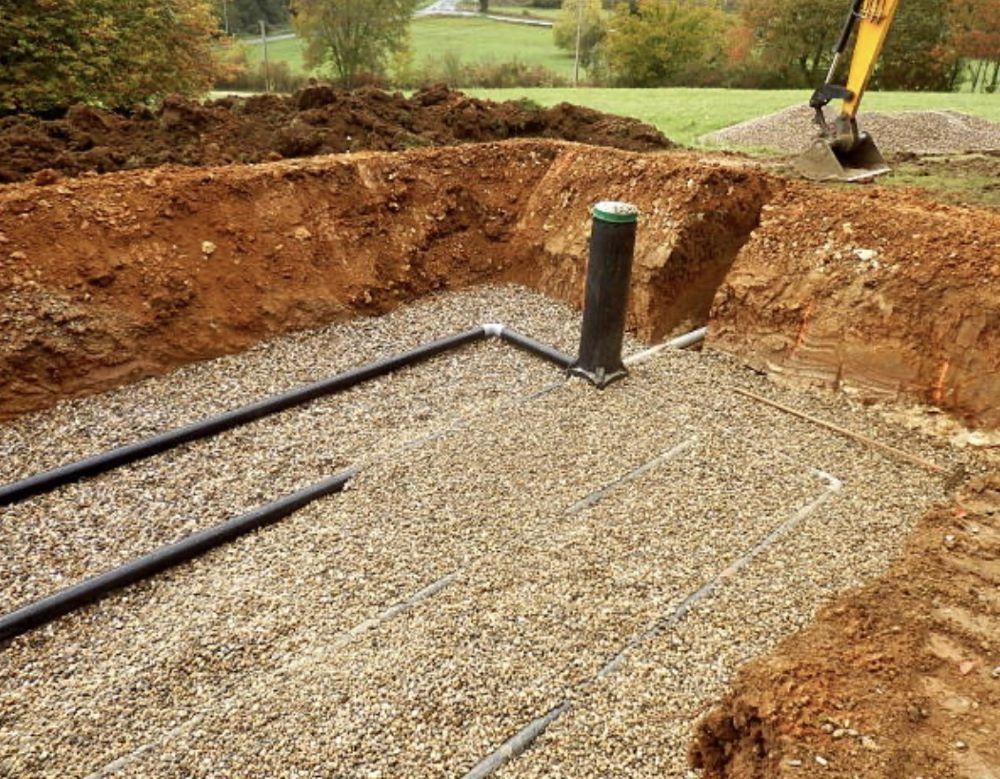 Construction site, a septic system installation, gravel bed with black pipes, and a tall vent pipe.