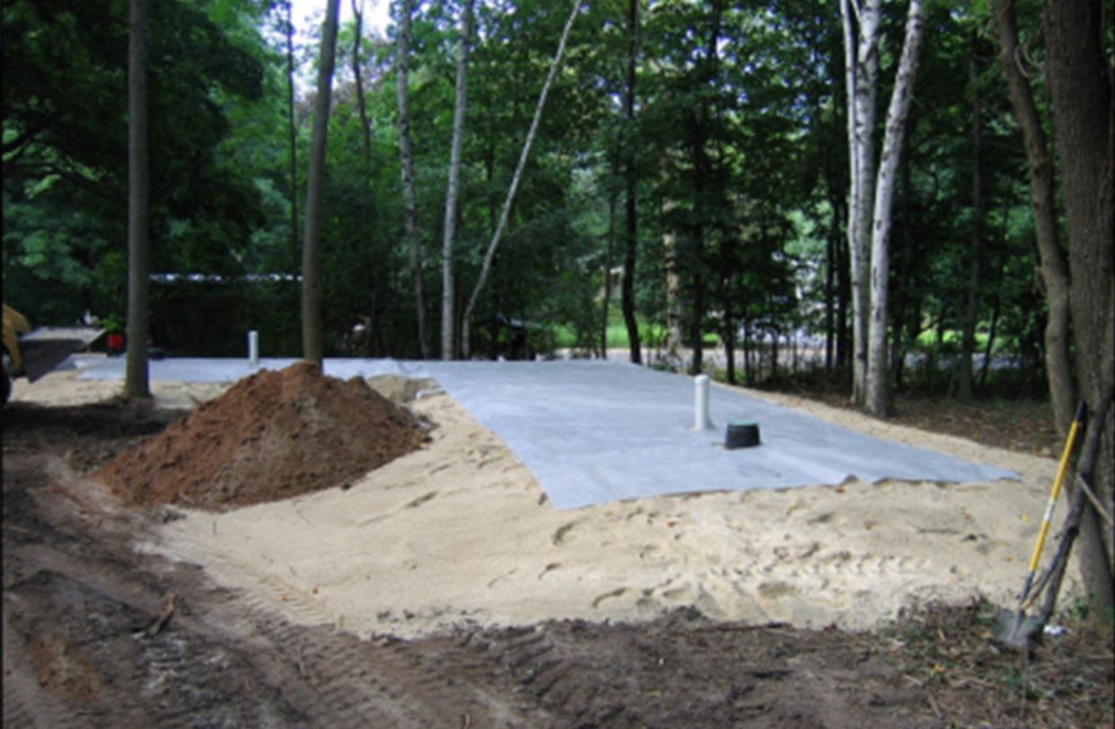 A gravel pad with sand and dirt is surrounded by trees in a wooded area.