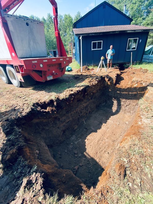 A trench is dug in a yard with a truck nearby, and two people are standing next to a blue house.