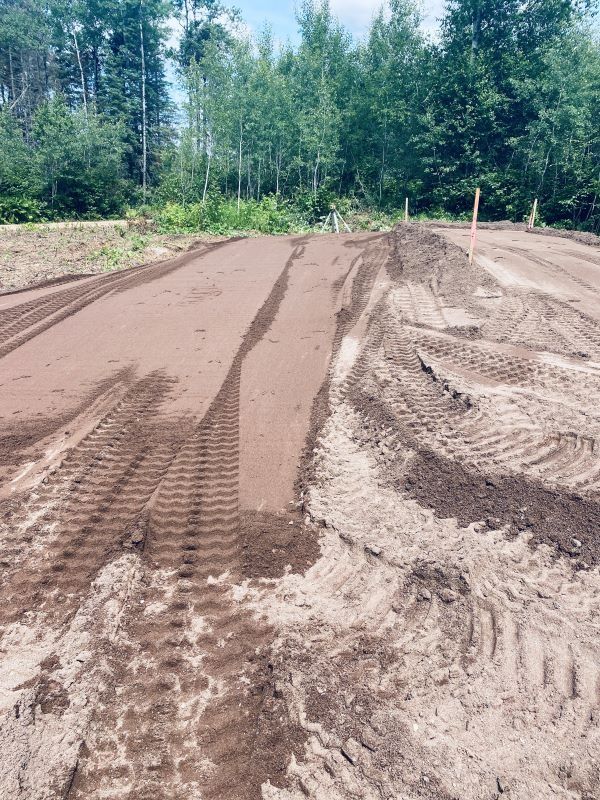 Prepared garden beds in a field, with tractor tracks in the sandy soil.