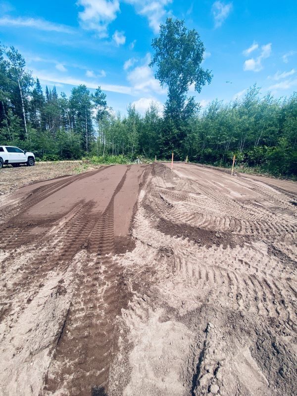 A dirt-covered clearing with tire tracks, possibly a construction site, under a partly cloudy sky; a white truck is visible.