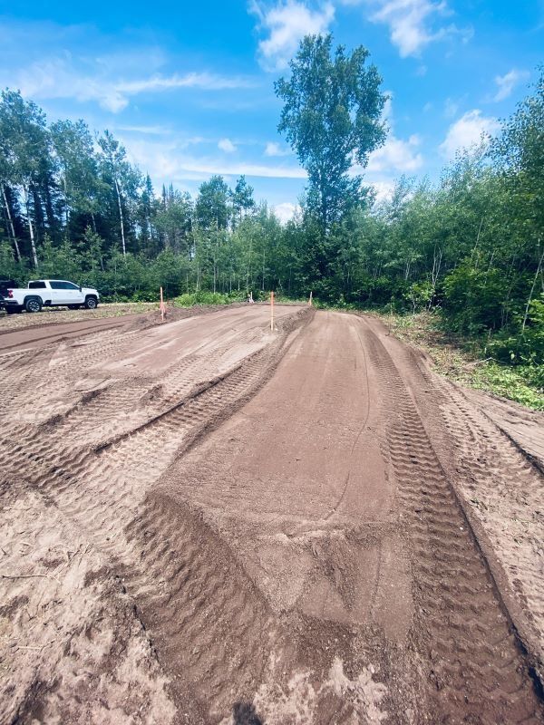 Dirt bike track under a blue sky; an empty track with groomed jumps, truck parked in the background.