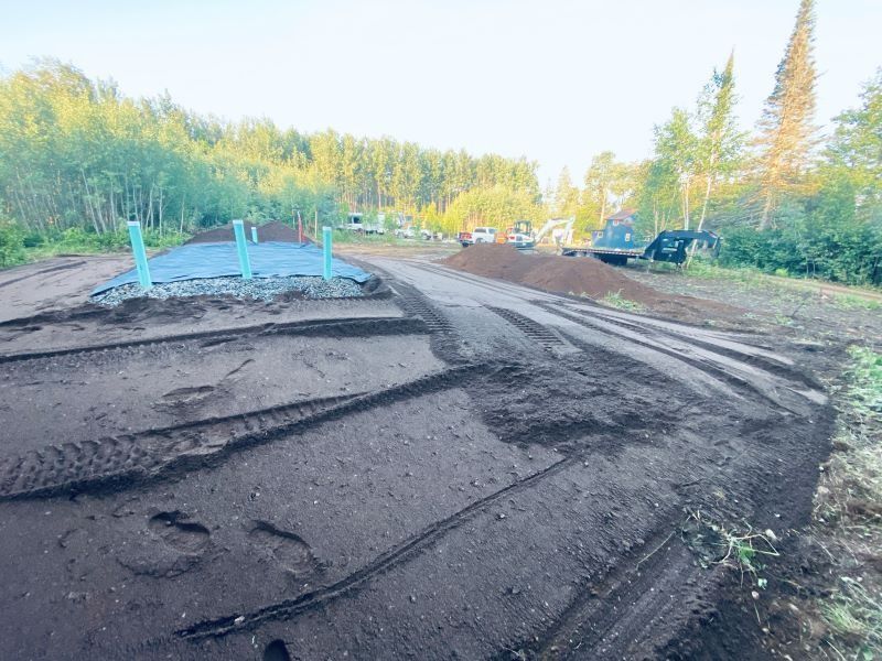 Dirt road construction with pipes, equipment, and trees in the background.