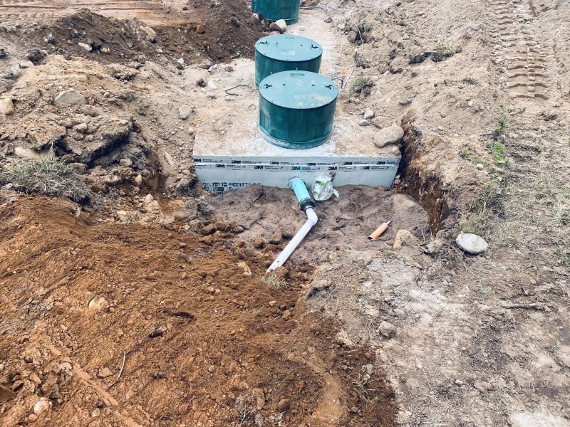 Septic system installation: green tanks and concrete box in a dirt trench.