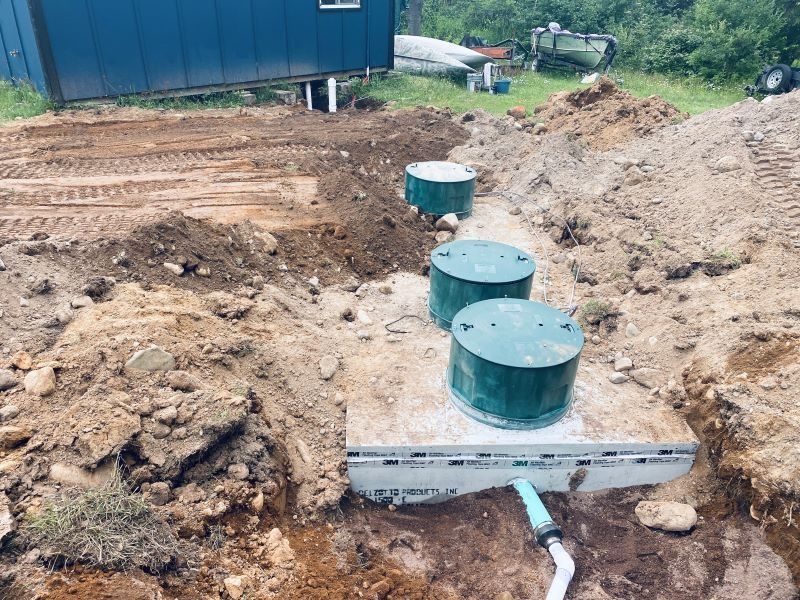 Three green septic tank lids and a concrete base in an open excavation.