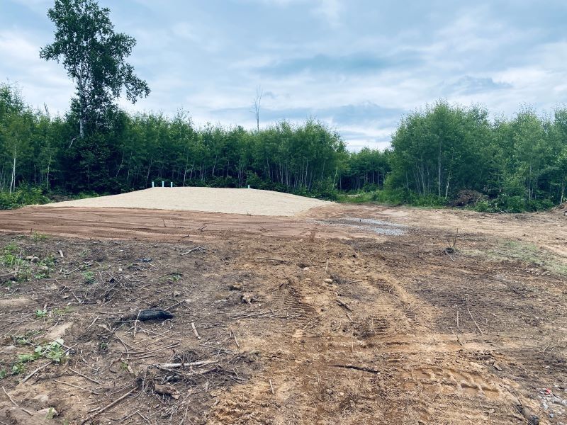 Dirt clearing with a mound of sand surrounded by trees under a cloudy sky.
