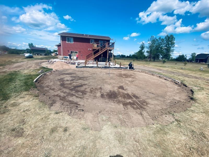 Backyard under construction. Red house with deck overlooks dirt area surrounded by landscaping.