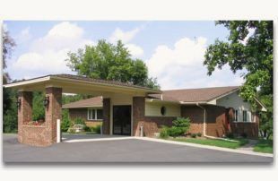 A cream-colored, multi-story funeral home with a stone-accented front and two cars parked in its asphalt lot.