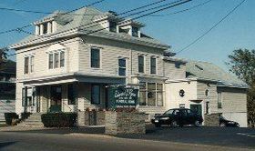 A cream-colored, multi-story funeral home with a stone-accented front and two cars parked in its asphalt lot.