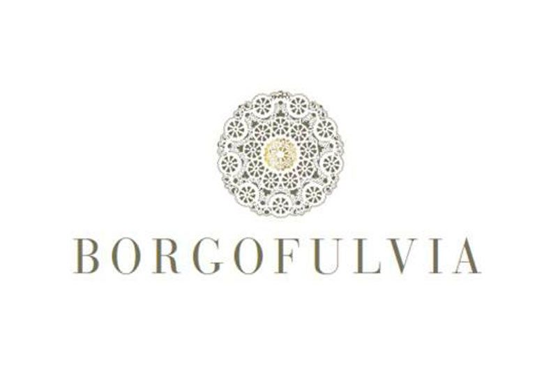 Logo per Borgofulvia. Disegno floreale dorato e beige sopra il nome in carattere beige.