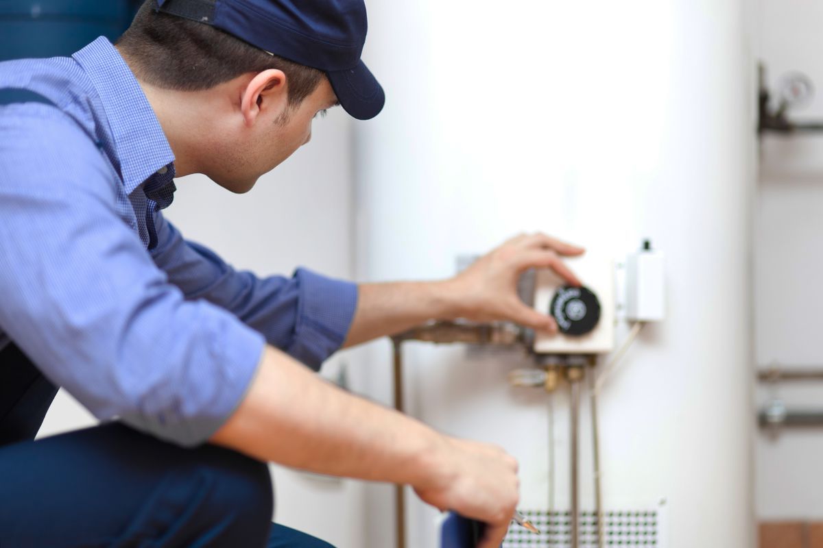 A man is fixing a water heater with a wrench.