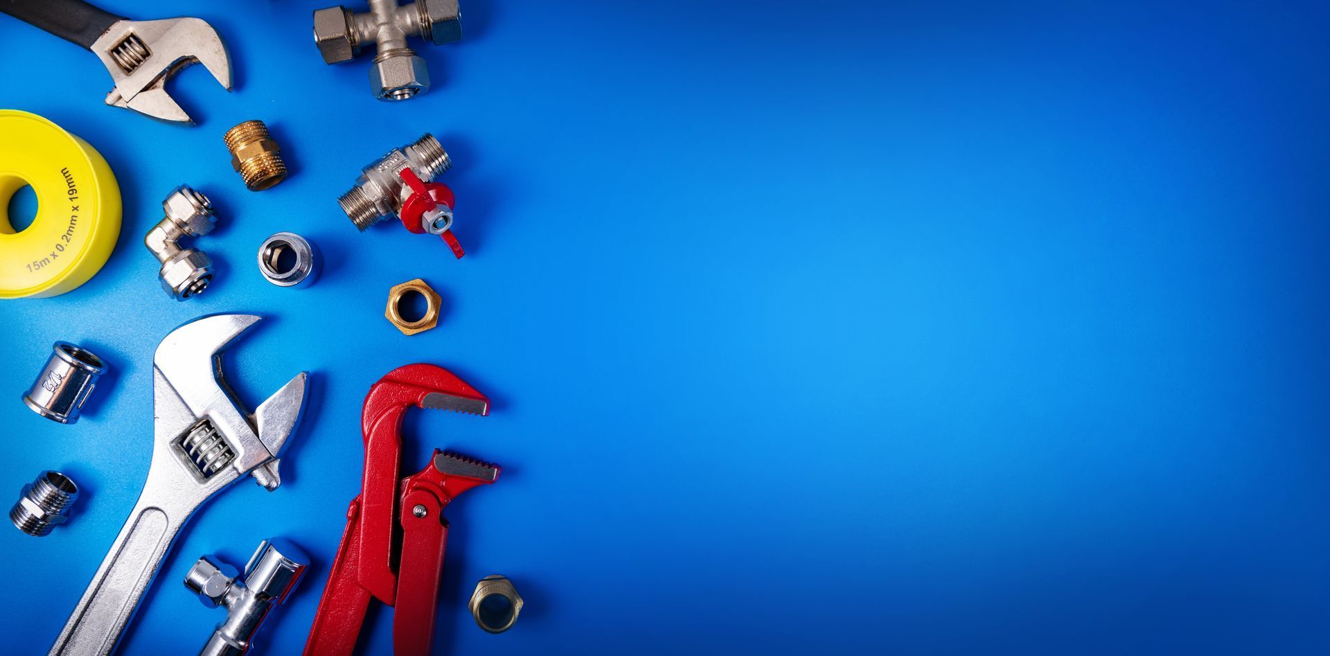 Plumbing tools and assorted metal pipe fittings arranged on a bright blue background.