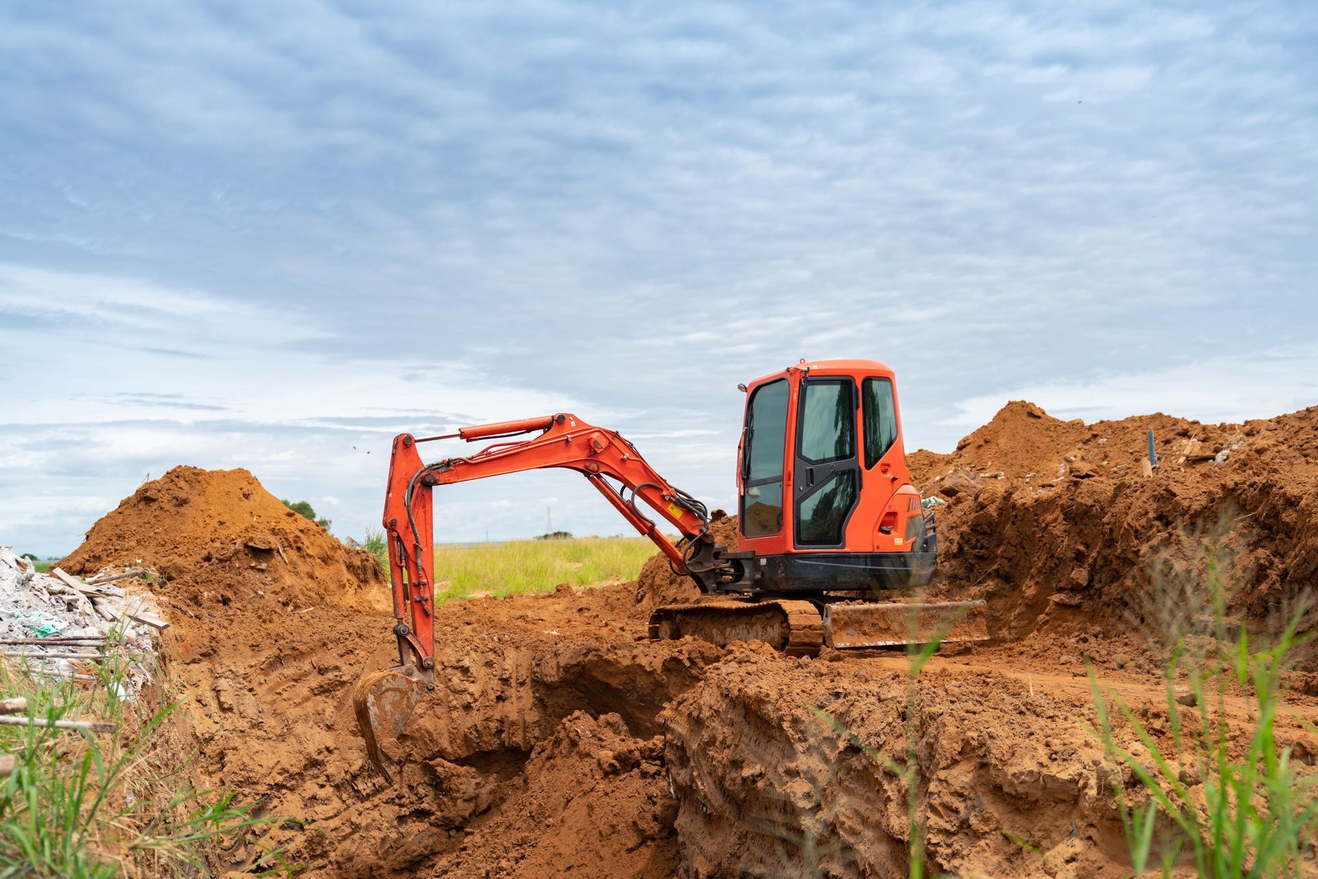 Orange excavator digging in brown earth under a cloudy sky.