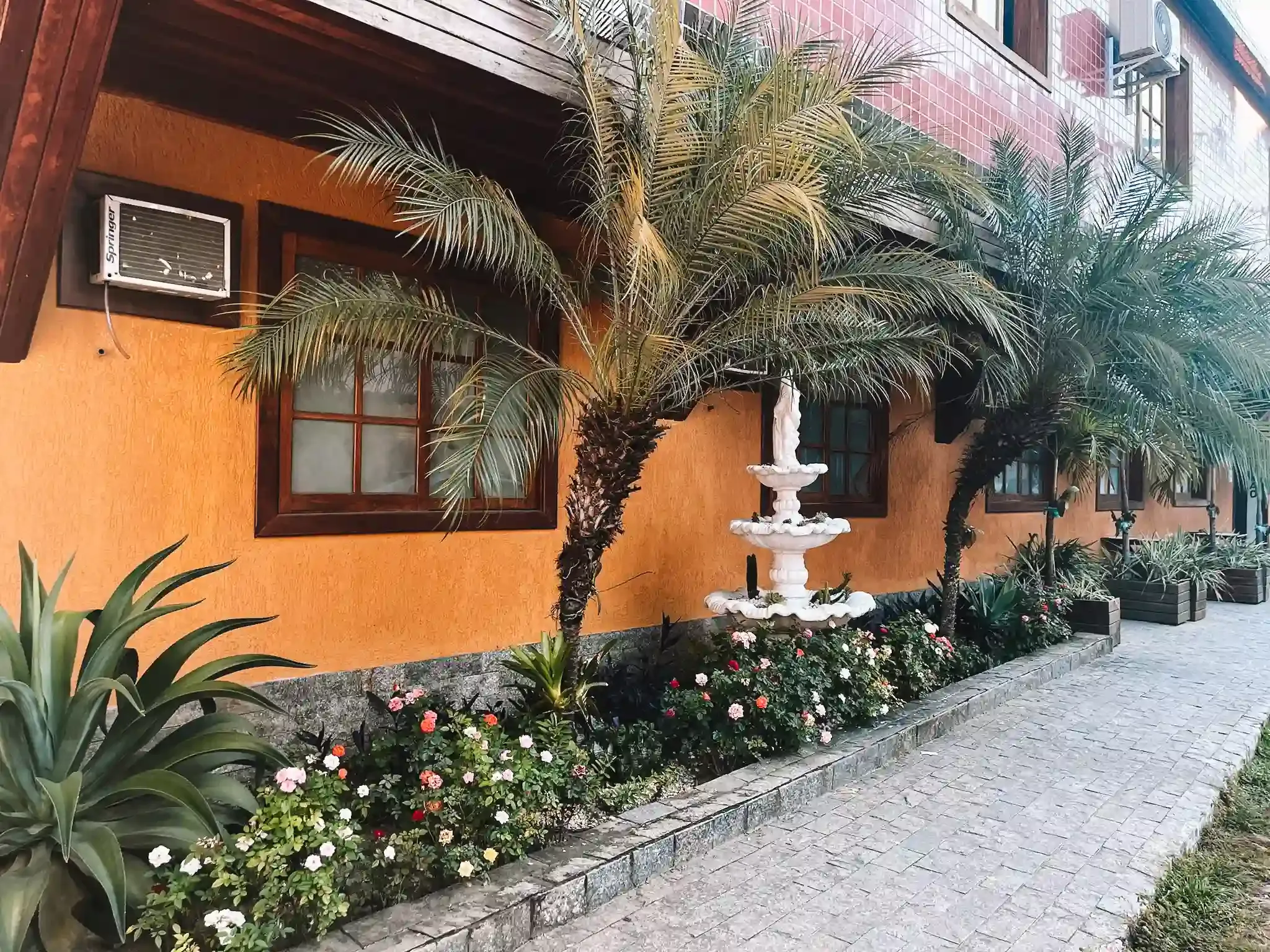 Um edifício com uma fonte na frente, cercado por flores e árvores.-pousada-itacuruca-inn