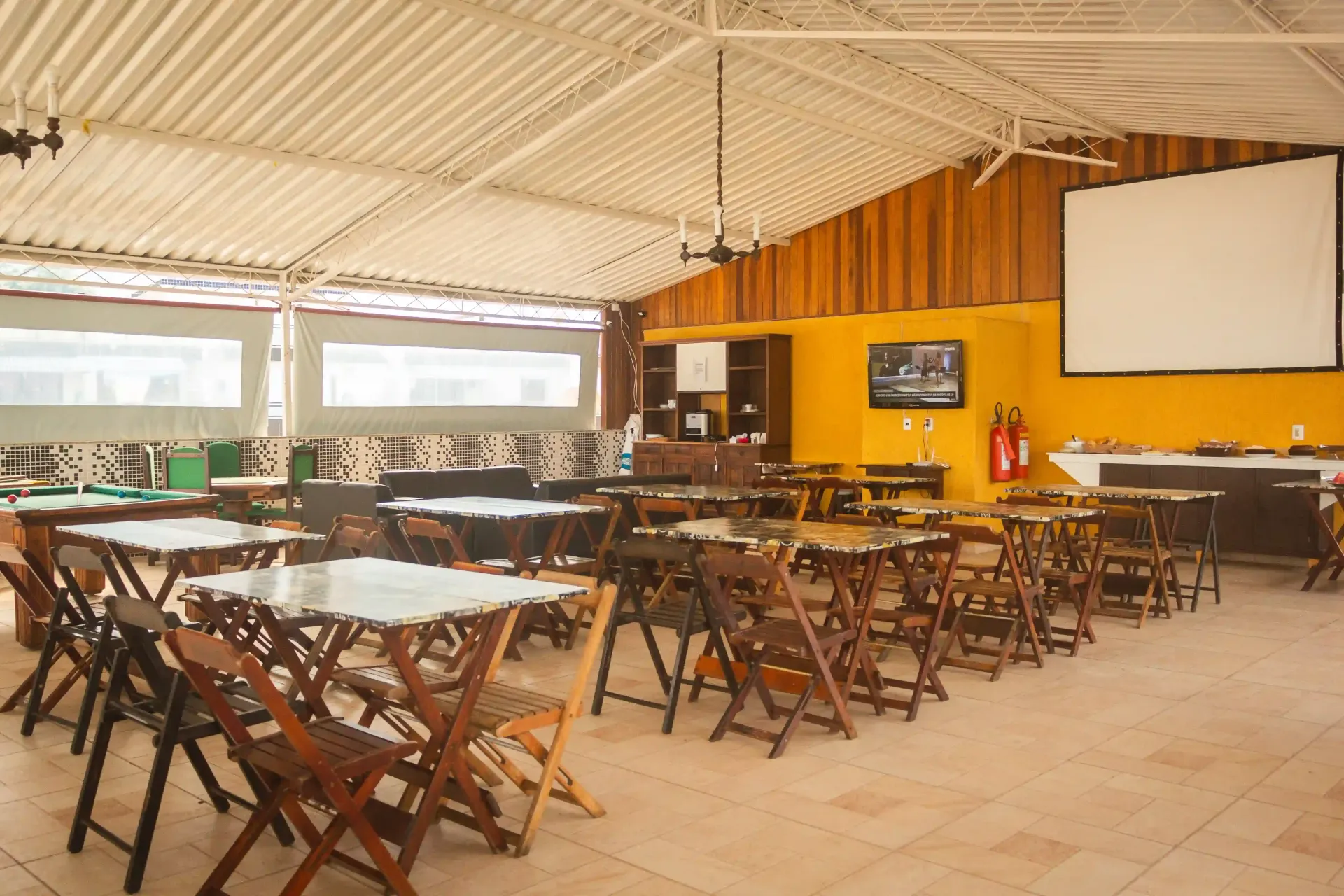 Uma sala grande com mesas e cadeiras e uma tela de projetor.-pousada-itacuruca-inn