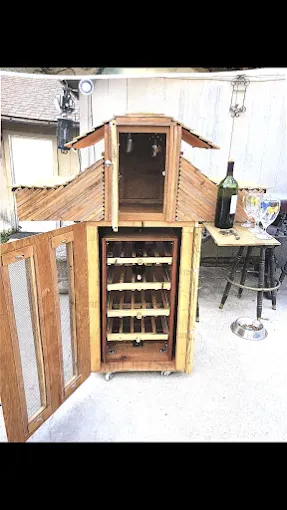 A wooden wine rack cabinet with glass-front doors, shelves for wine bottles, and a top compartment on a patio.