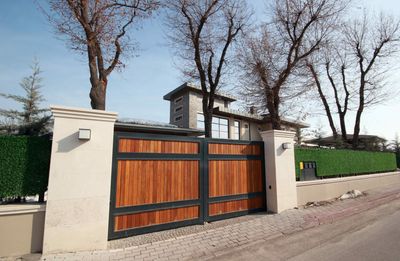 A wooden gate is leading to a house with trees in the background.