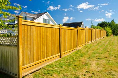 A wooden fence surrounds a lush green yard in front of a house.