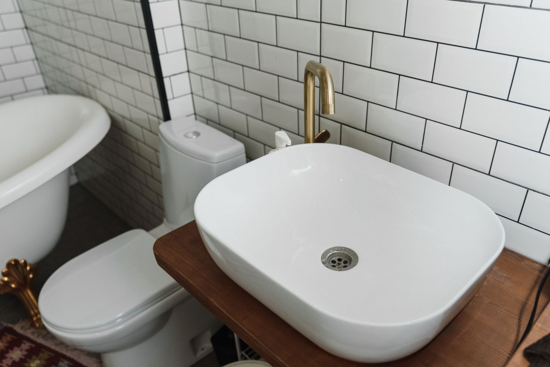 Small bathroom sink with brass faucet beside a toilet and bathtub against white subway tile walls