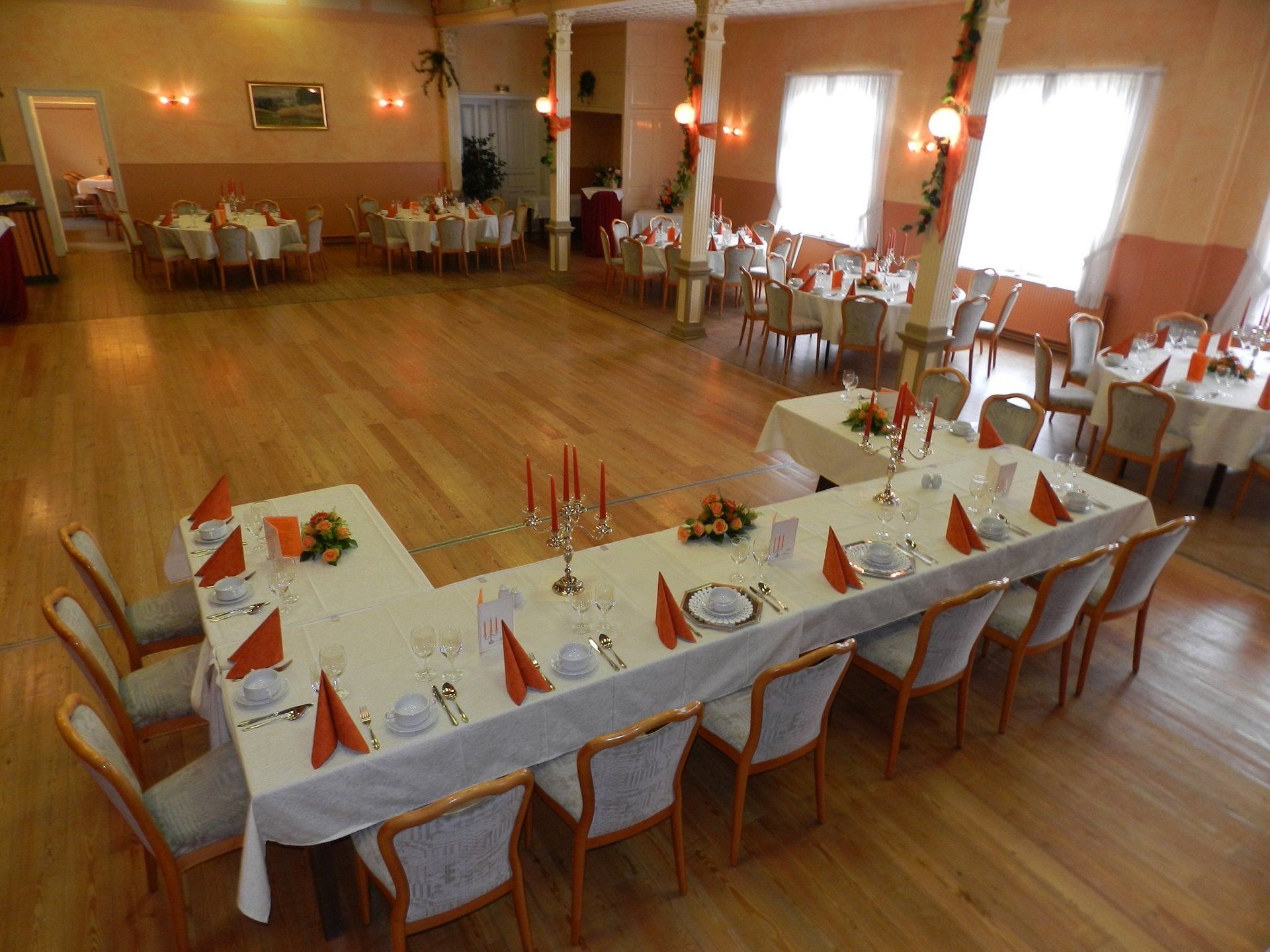 Großer Bankettsaal mit mehreren gedeckten Tischen. Holzböden, helle Wände und formelles Gedeck.