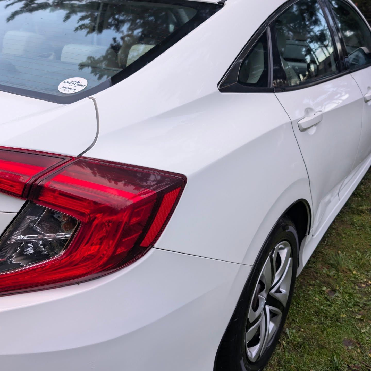 Woman in straw hat smiles, holding wine glass near a lake.