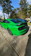 A vibrant green Ford Mustang parked on a concrete driveway with a blue car in the background.