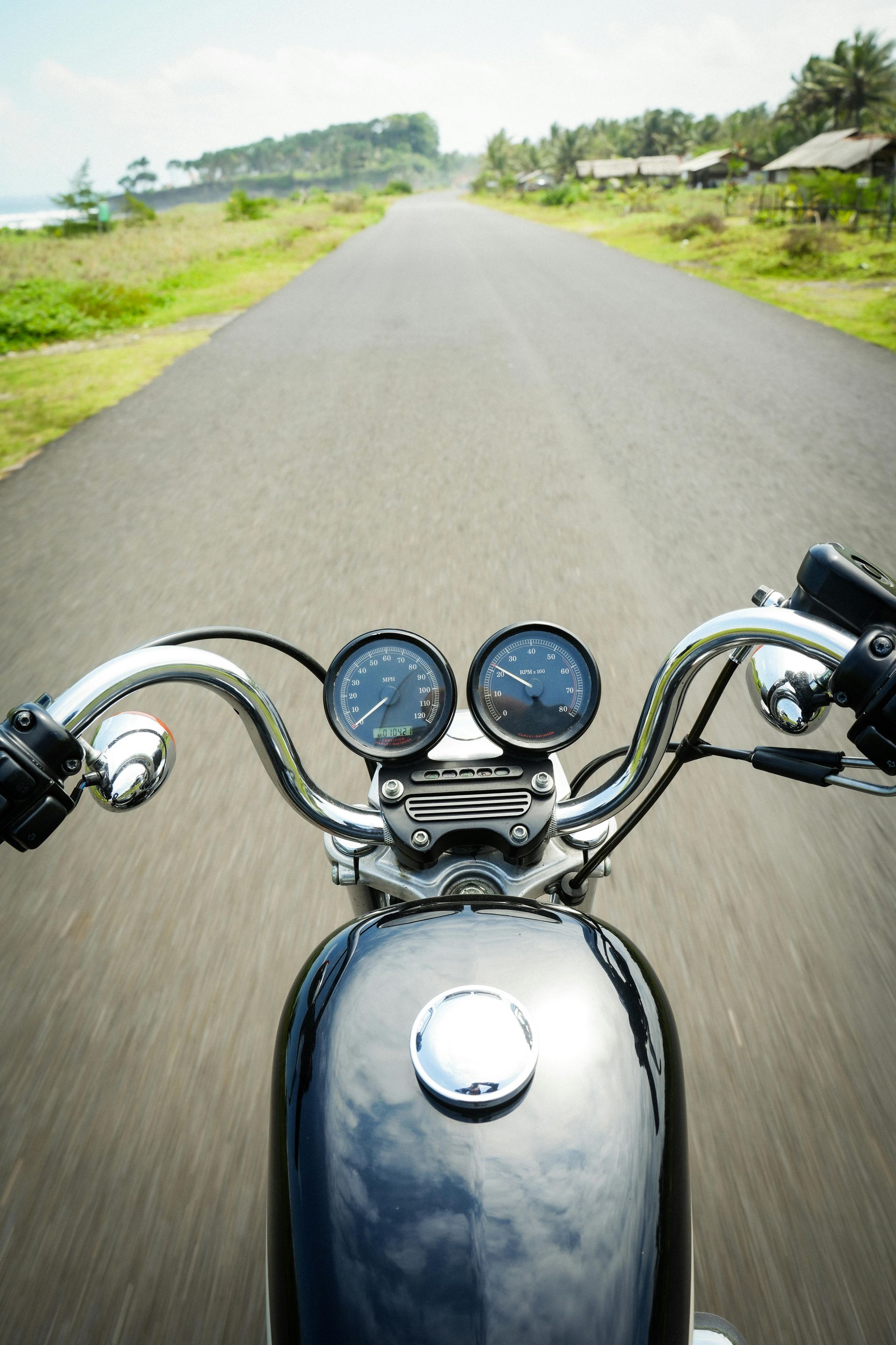 Woman in straw hat smiles, holding wine glass near a lake.