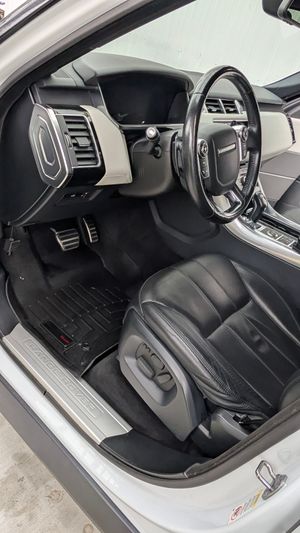 The driver-side interior of a vehicle featuring black leather seats, a steering wheel, and a branded silver door sill.