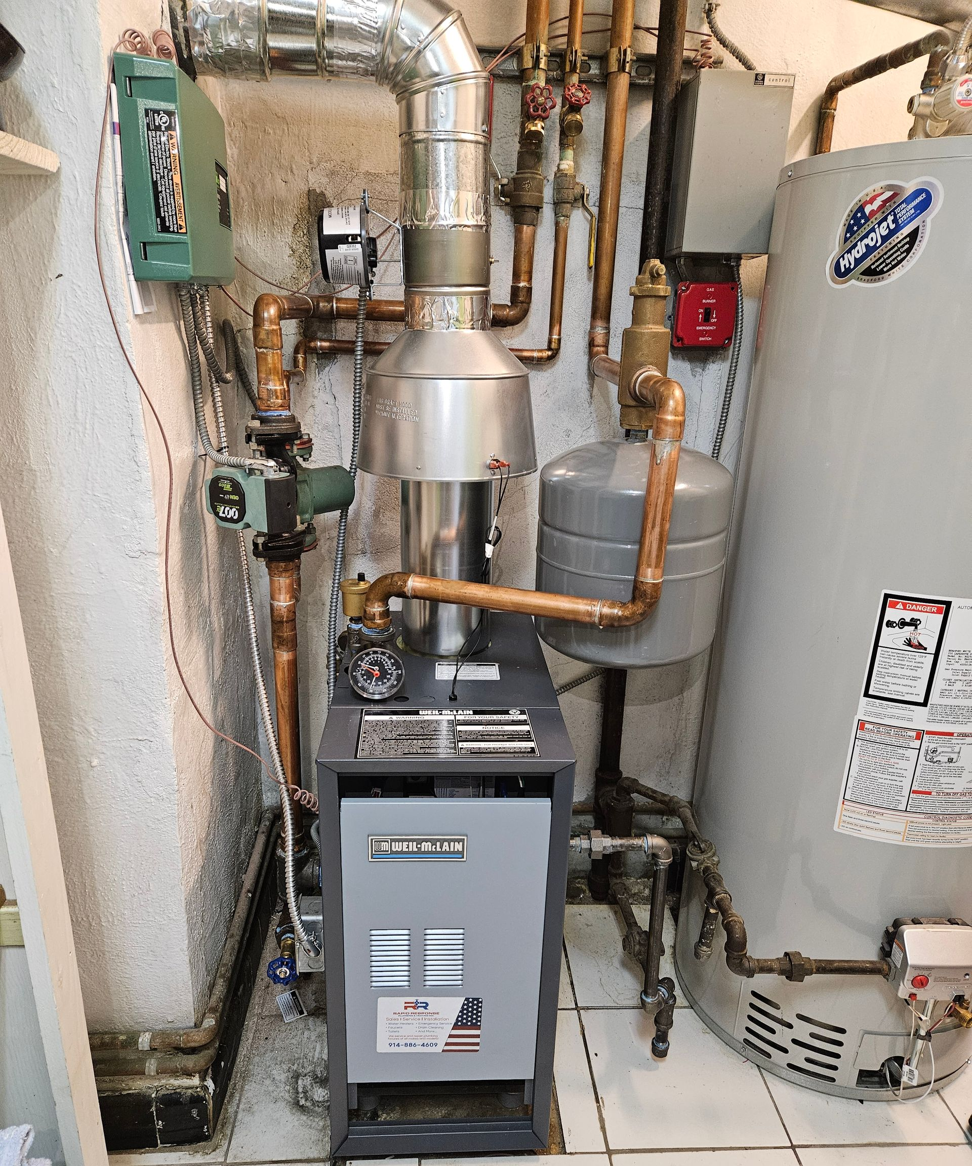 A boiler with connected pipes, a water tank, and other plumbing fixtures in a utility room.