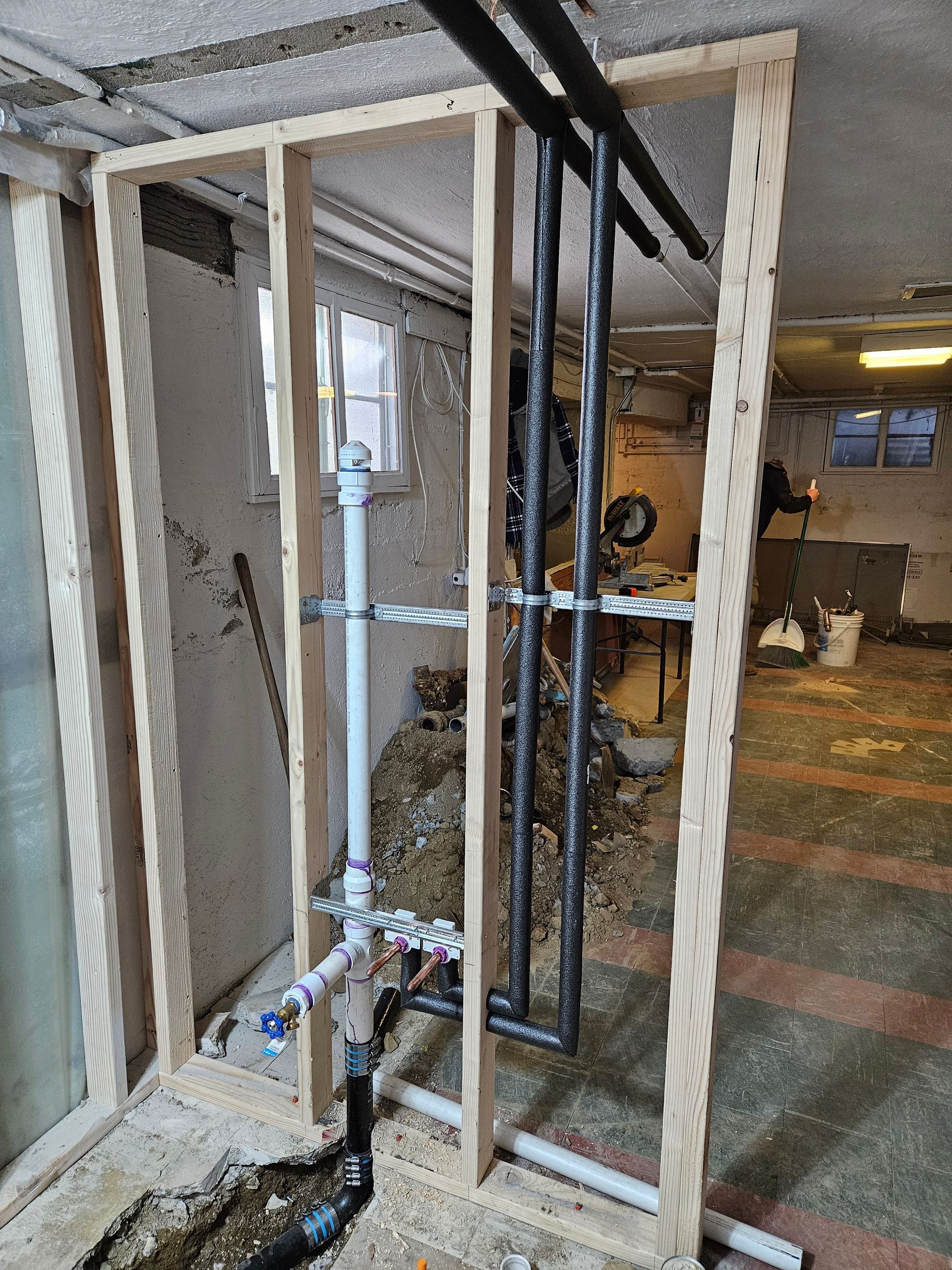 Framing for pipes in basement, including black and white pipes against a partially finished wall.