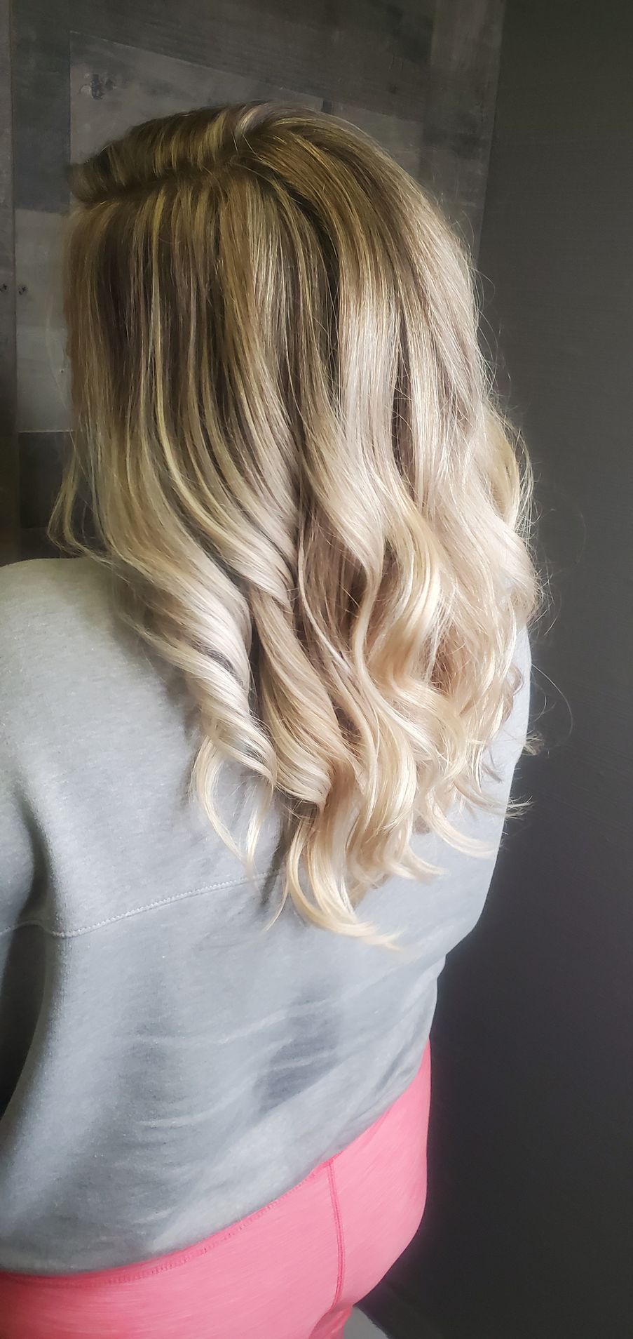 A woman with long blonde hair is wearing a gray sweater and pink pants.