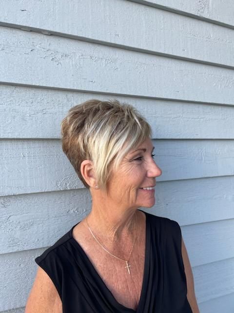 A woman with short blonde hair is standing in front of a white wall.