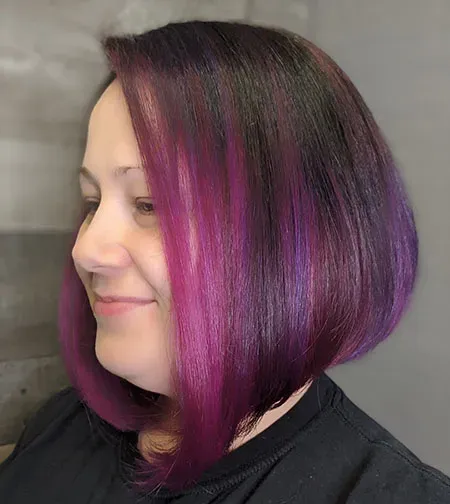 A woman with purple hair is wearing a black shirt and smiling.