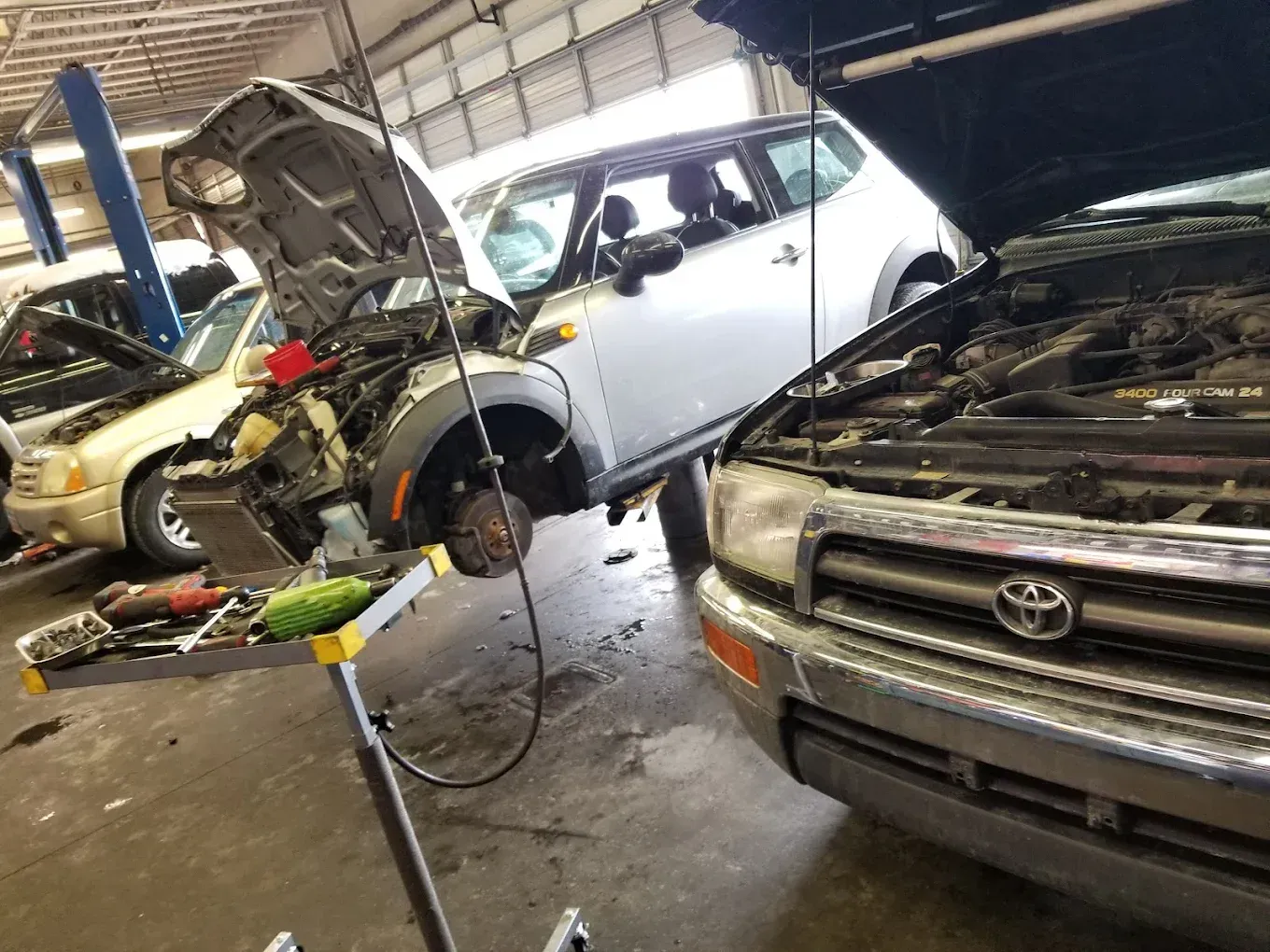 Auto repair shop with several cars, one hood open and tools on the floor; mechanic working on a white car. | Jones Complete Car Care