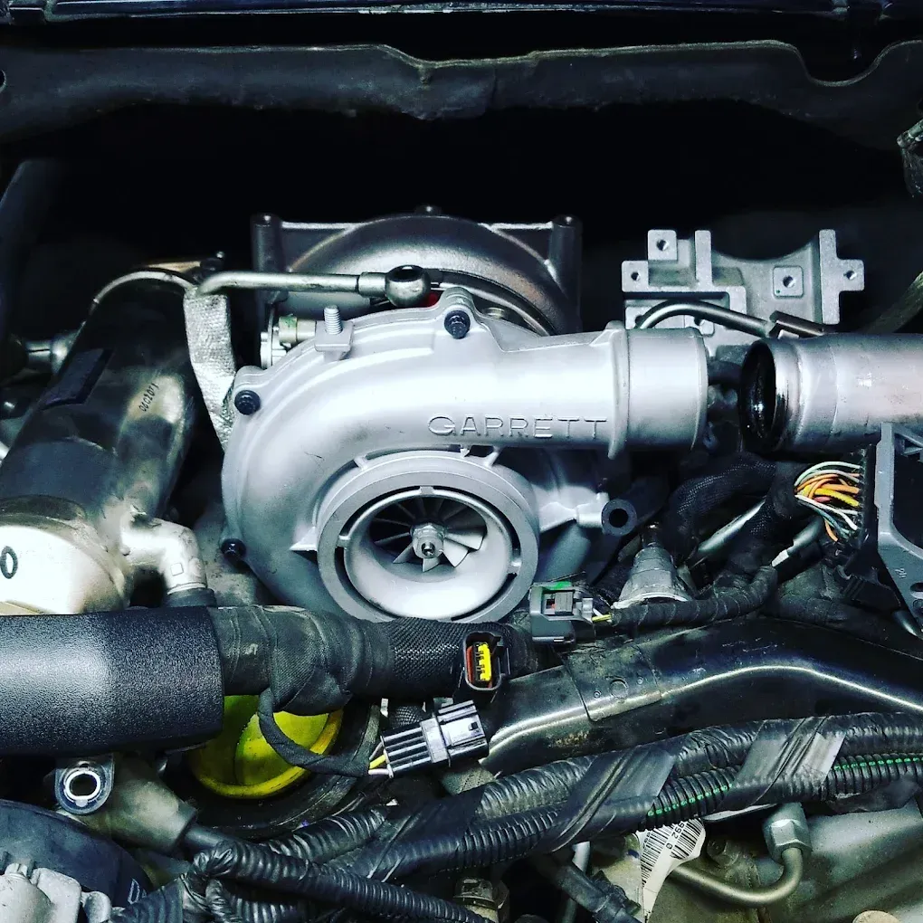 Car engine bay with a visible turbocharger and intake piping, surrounded by wiring and hoses. | Jones Complete Car Care