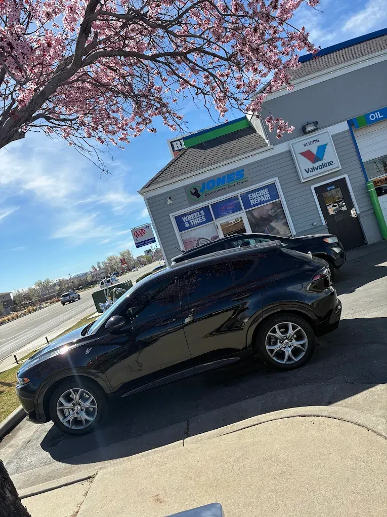 Black SUV parked outside a small storefront on a sunny street with a blooming tree overhead | Jones Complete Car Care
