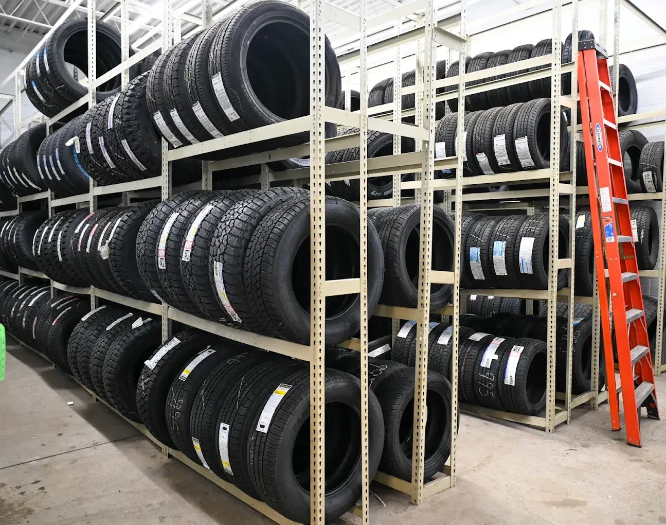 Rows of black tires stacked on metal warehouse shelves beside an orange ladder | Jones Complete Car Care