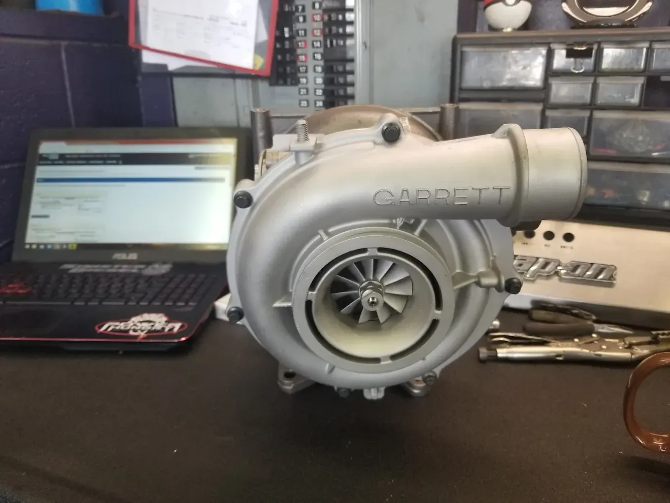 Silver turbocharger on a workbench with a laptop and tools in the background | Jones Complete Car Care