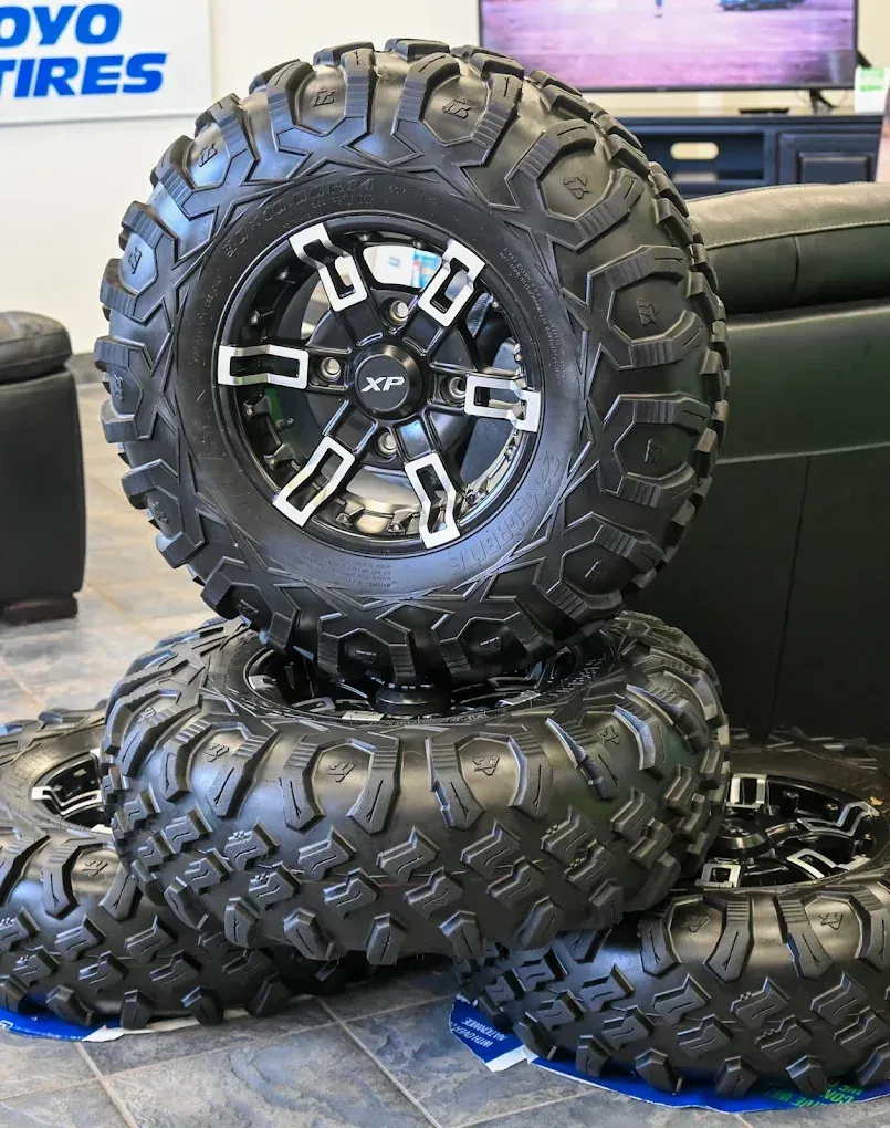 Stack of three rugged off-road tires with black and silver rims on a showroom floor. | Jones Complete Car Care