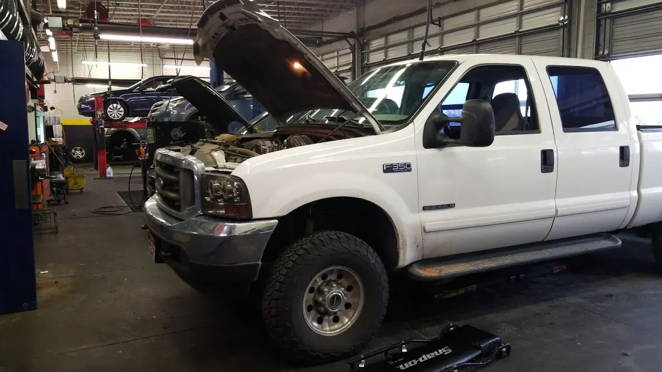 White pickup truck in a repair shop with hood open, mechanic working on a black SUV in the background. | Jones Complete Car Care