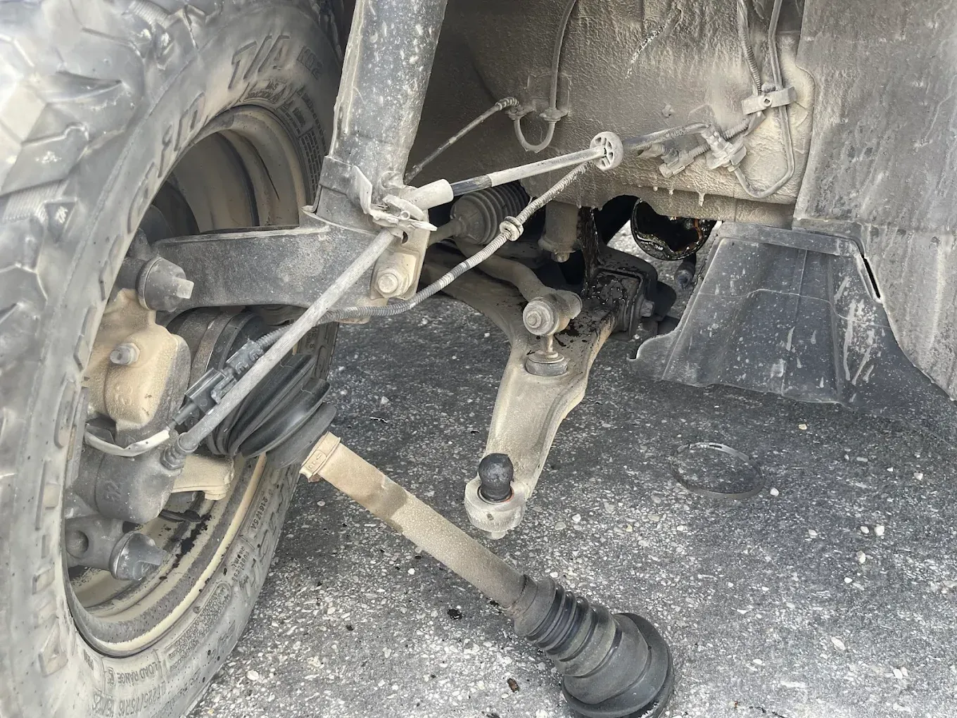 Close-up of a vehicle’s front wheel and steering suspension with a detached axle on a dirt surface. | Jones Complete Car Care
