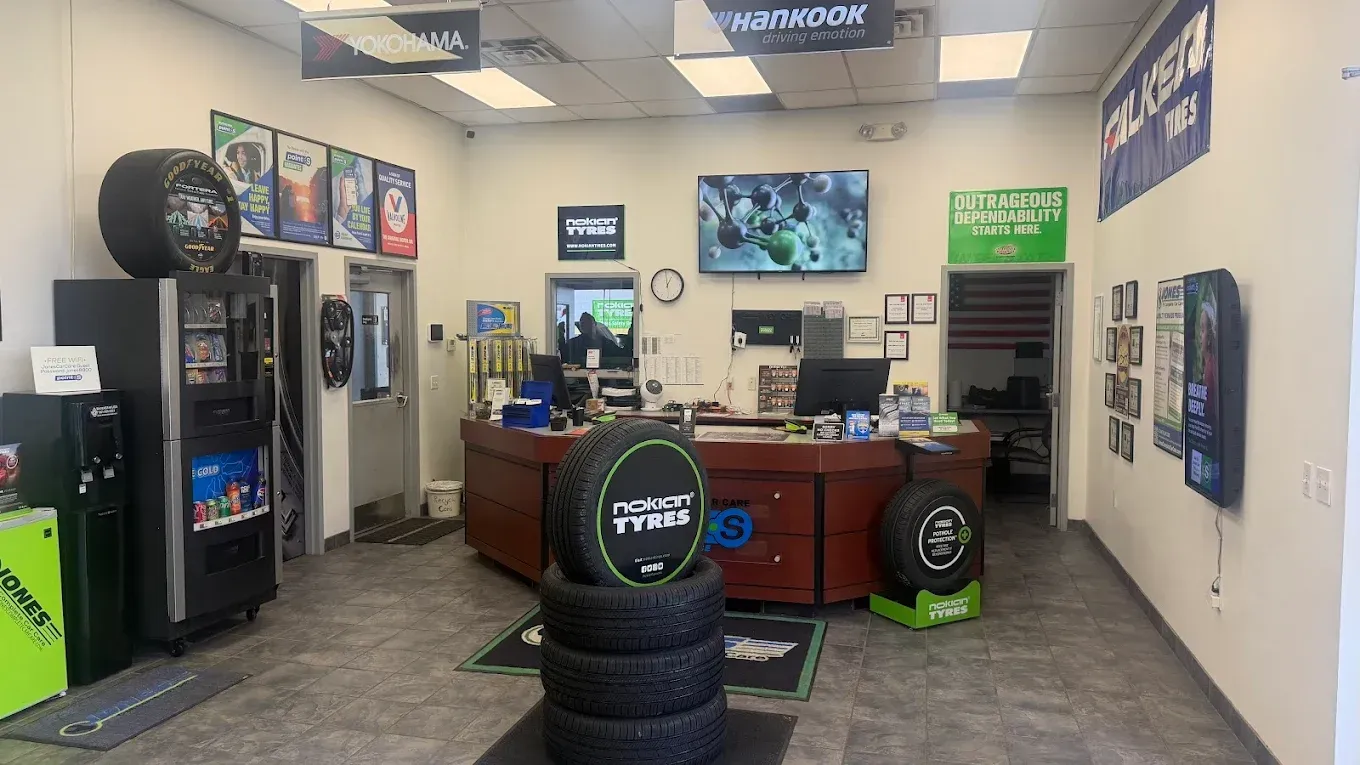 Tire shop waiting area with service desk, TV, vending machines, and stacked tires in the foreground | Jones Complete Car Care