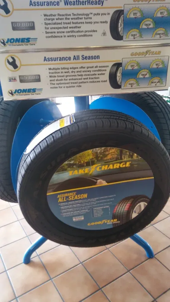 Two stacked tire display signs above a black tire on a blue stand in a tiled shop aisle | Jones Complete Car Care