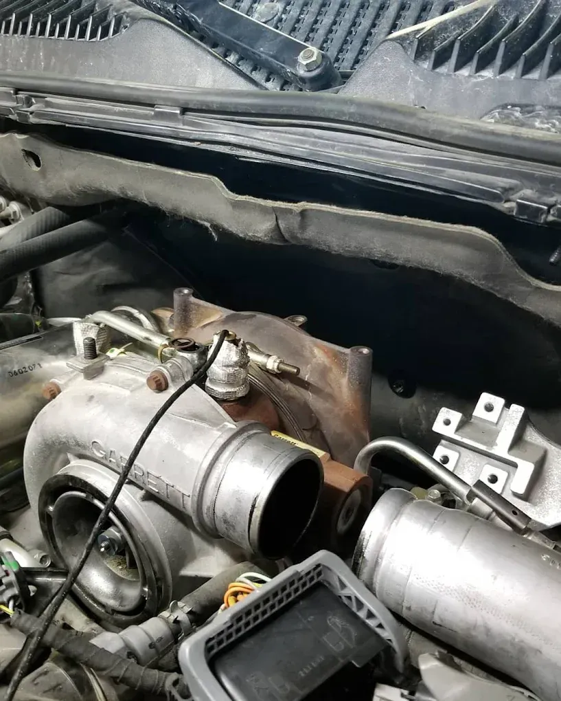 Car engine with exposed turbo and metal piping under the hood, showing mechanical parts and wiring. | Jones Complete Car Care