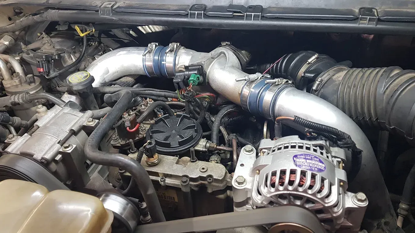 Car engine bay with polished intake piping, turbo components, and alternator visible | Jones Complete Car Care