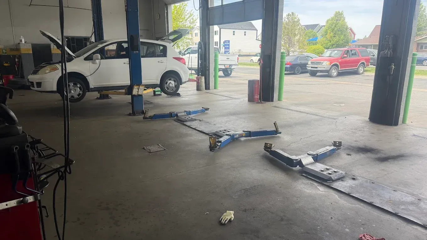Damaged car parts scattered on a garage floor with a white SUV on a lift in the background | Jones Complete Car Care