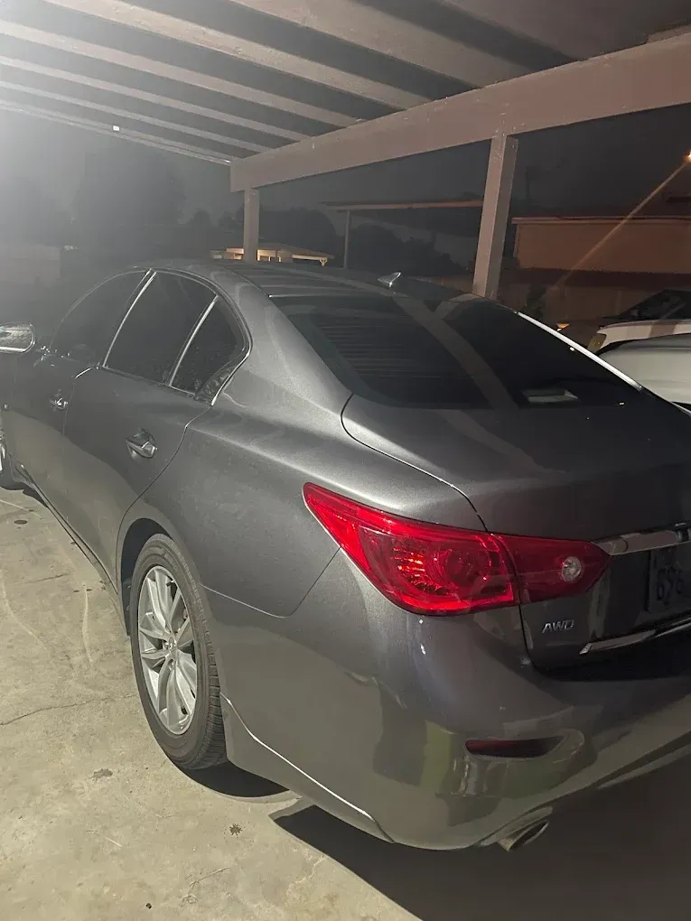 Gray sedan parked under a carport at night, rear-left view with red tail lights visible | Jones Complete Car Care