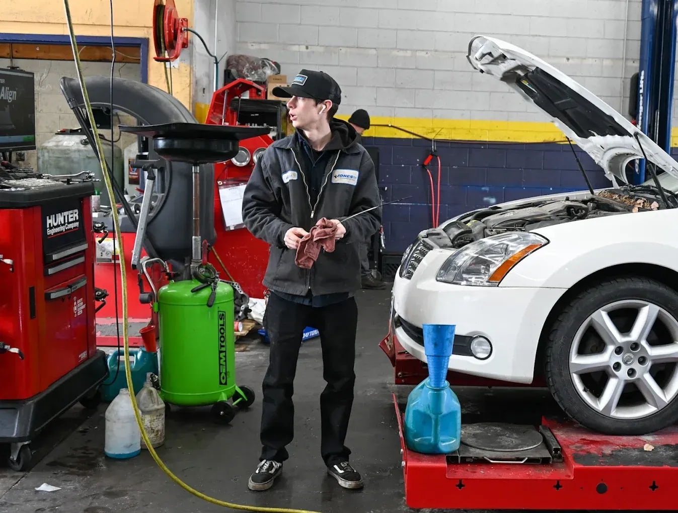 Mechanic in auto shop beside a white car on a lift, with tools and hood open. | Jones Complete Car Care