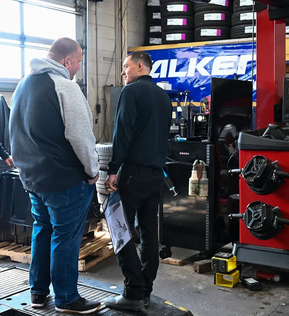 Two men talking in a tire shop beside stacked tires and a red tool cabinet | Jones Complete Car Care