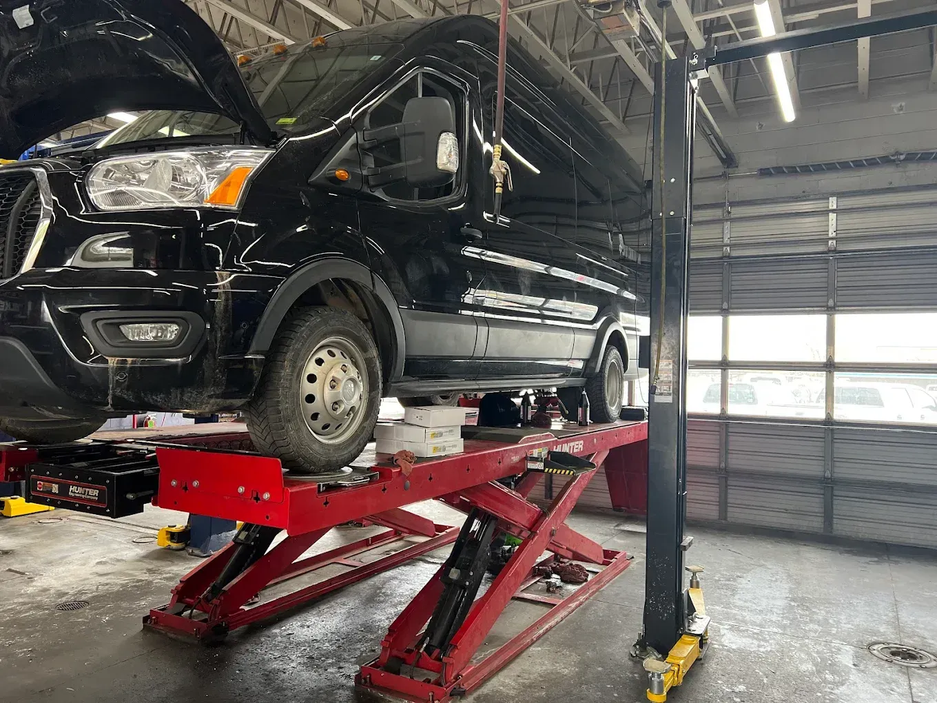 Black van lifted on a red hydraulic car lift in a garage workshop | Jones Complete Car Care